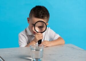 little boy looking through magnifying glass at cup of water