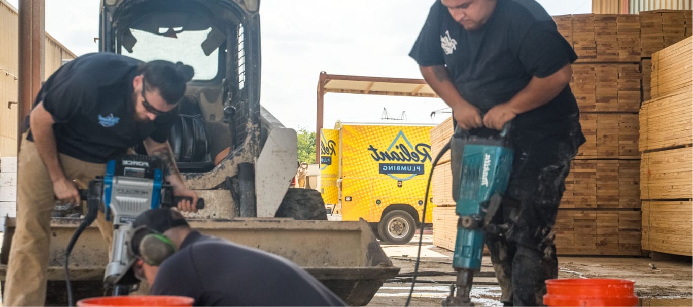 Two plumbers using jackhammers on concrete