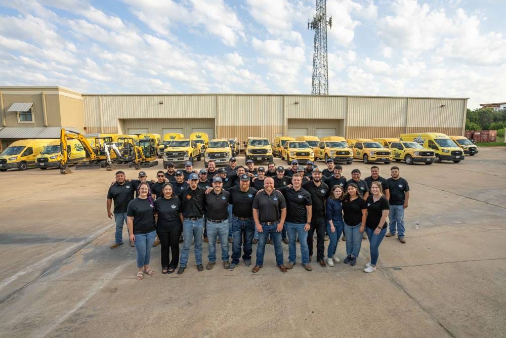 Reliant Plumbing Austin team standing in front of fleet of trucks and warehouse