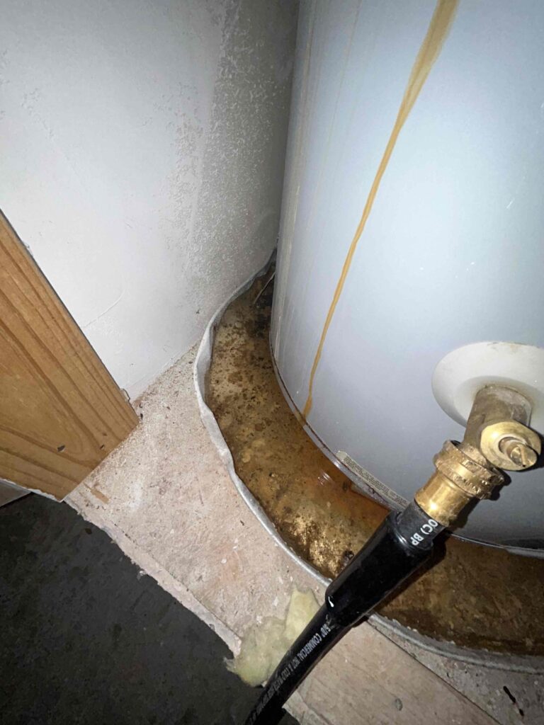old leaking water heater and drip pan filled with dirty water