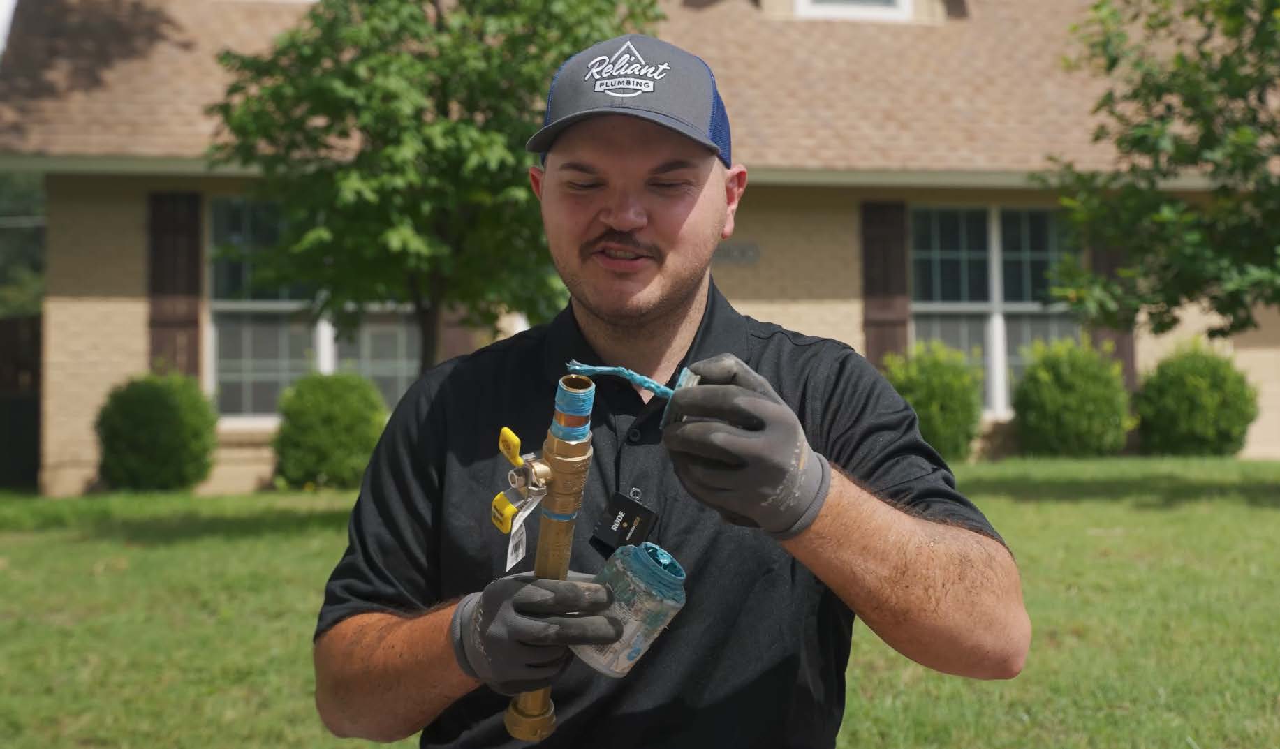 prepare-the-threads Reliant Plumbing technician applying pipe thread sealant to a brass fitting during an outdoor plumbing installation in front of a brick home in Austin, Texas.