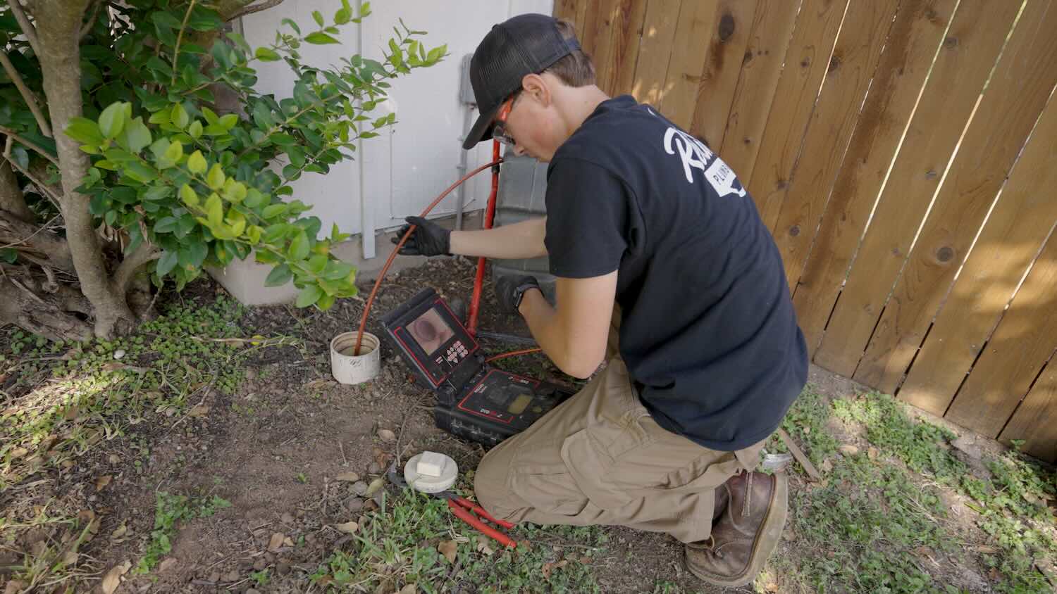Plumber performing a sewer camera inspection through an outdoor cleanout, using a video monitor to inspect the condition of the underground pipe.