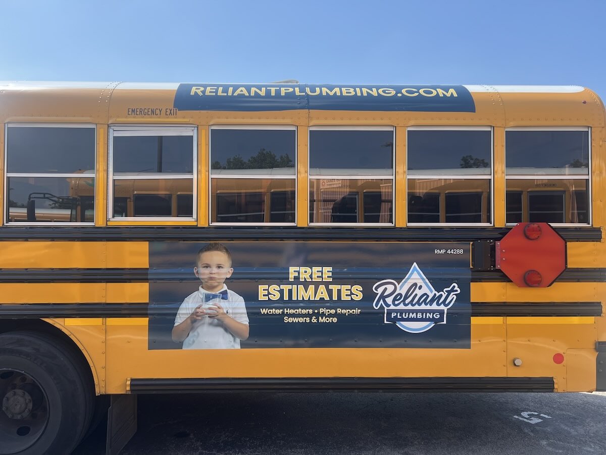 Yellow school bus featuring a Reliant Plumbing advertisement that includes a young child holding a wrench and text promoting free estimates; the poster is part of Reliant’s sponsorship in support of the Eanes Education Foundation.