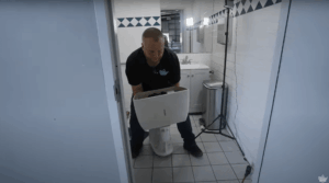 a plumber carrying an old toilet out of a bathroom