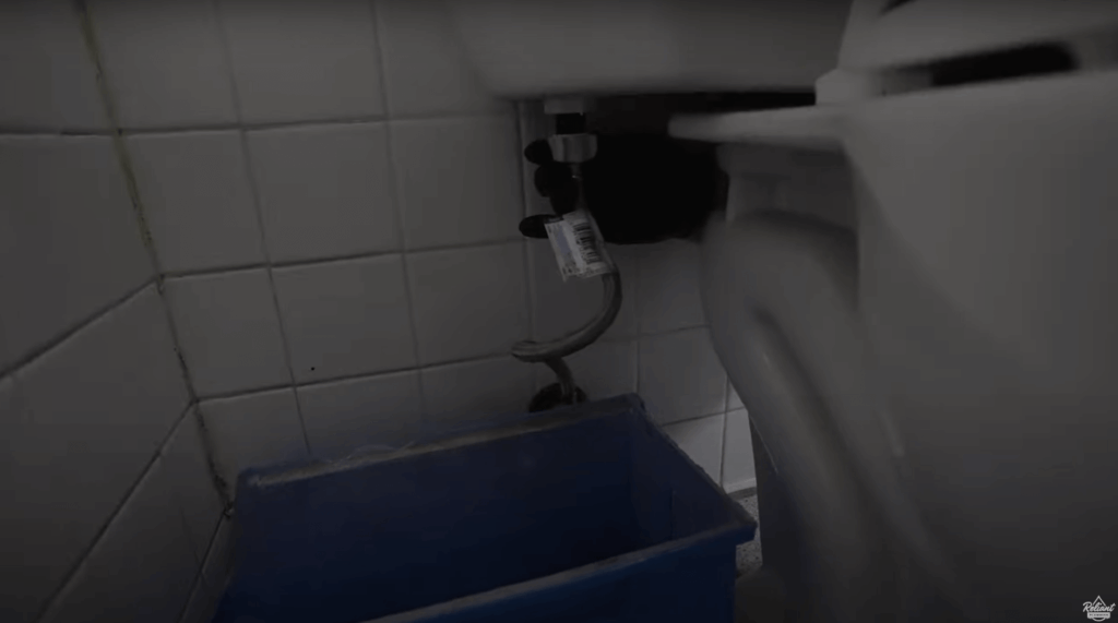 plumber unscrewing the plumbing supply line from beneath the toilet