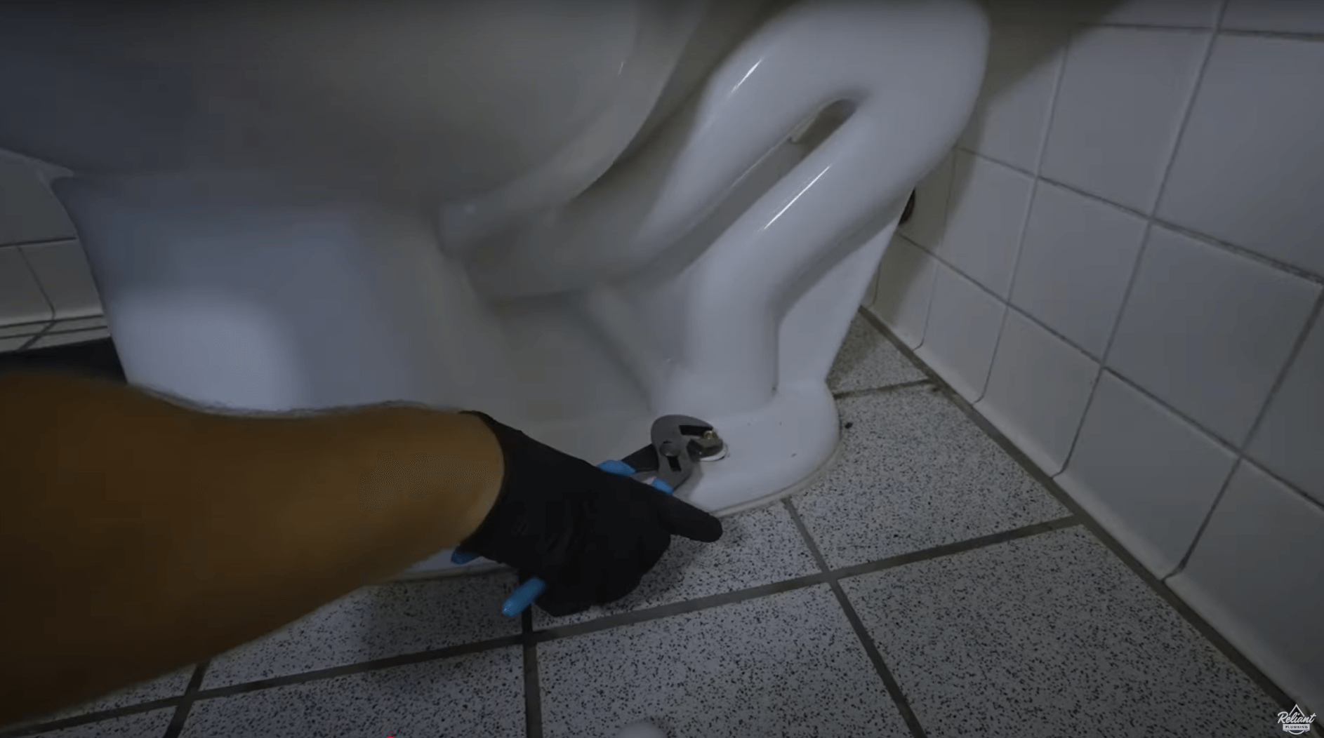 plumber unscrewing the bolts at the base of a toilet with a wrench