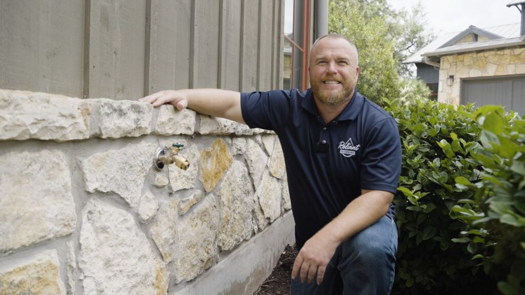 max hicks smiling crouched down next to a stone wall with a newly installed hose bib