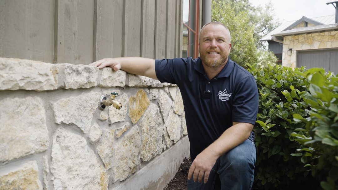 Max8 max hicks smiling crouched down next to a stone wall with a newly installed hose bib