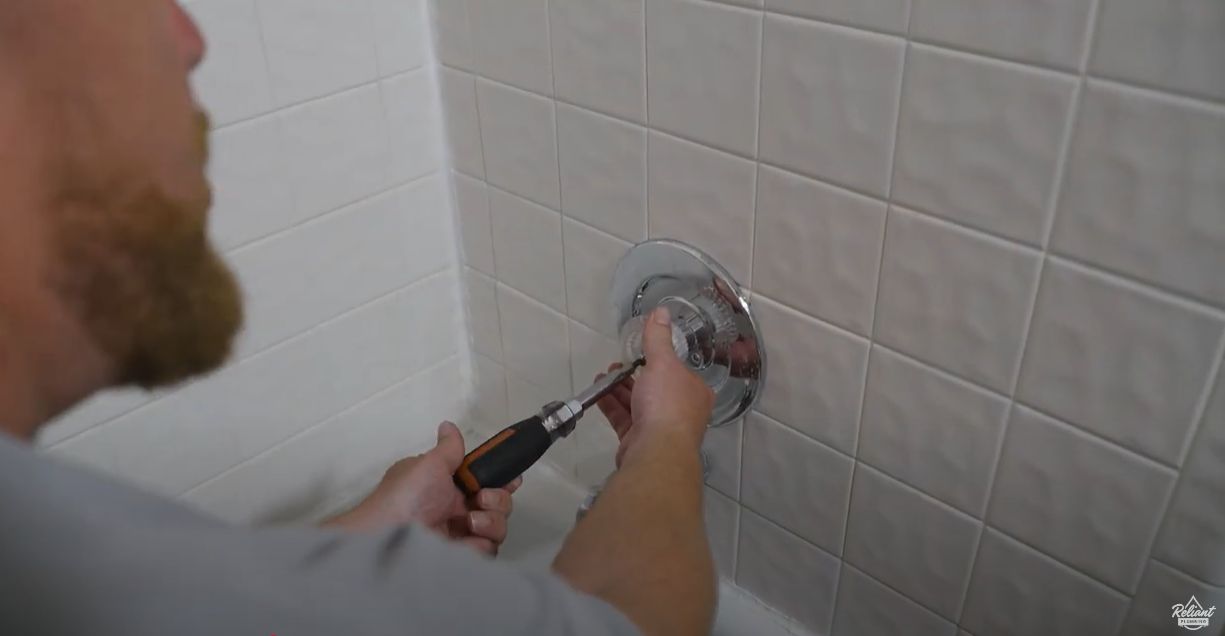 plumber unscrews the shower handle with a screwdriver