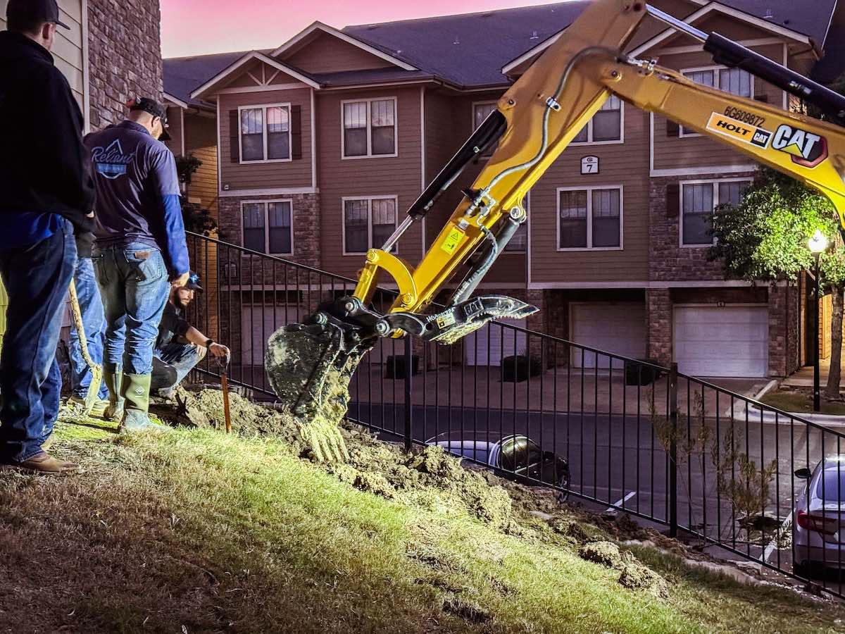 multifamily residential plumbing leak plumbers using excavator to dig up main water line at an apartment complex