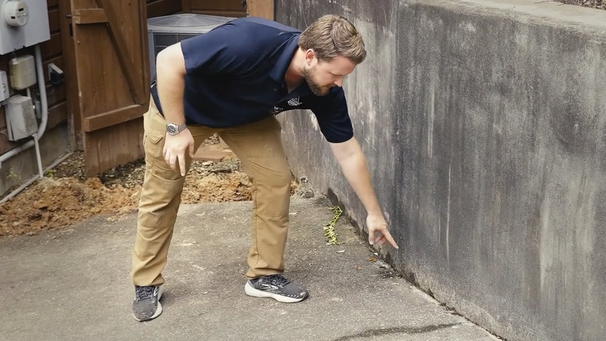 Reliant Plumbing technician Jacob points to a suspected water leak along the base of a concrete wall during a leak detection inspection.