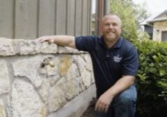 max hicks smiling crouched down next to a stone wall with a newly installed hose bib