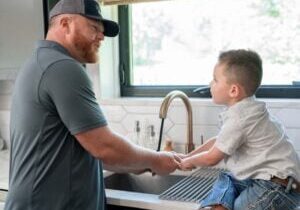 plumber in a residential home interacting with young son sitting at the sink learning about plumbing fictures