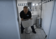 a plumber carrying an old toilet out of a bathroom