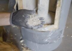 A gloved hand holding a pile of white, chalky sediment removed from the inside of a cut-open water heater, showing calcium buildup caused by hard water.
