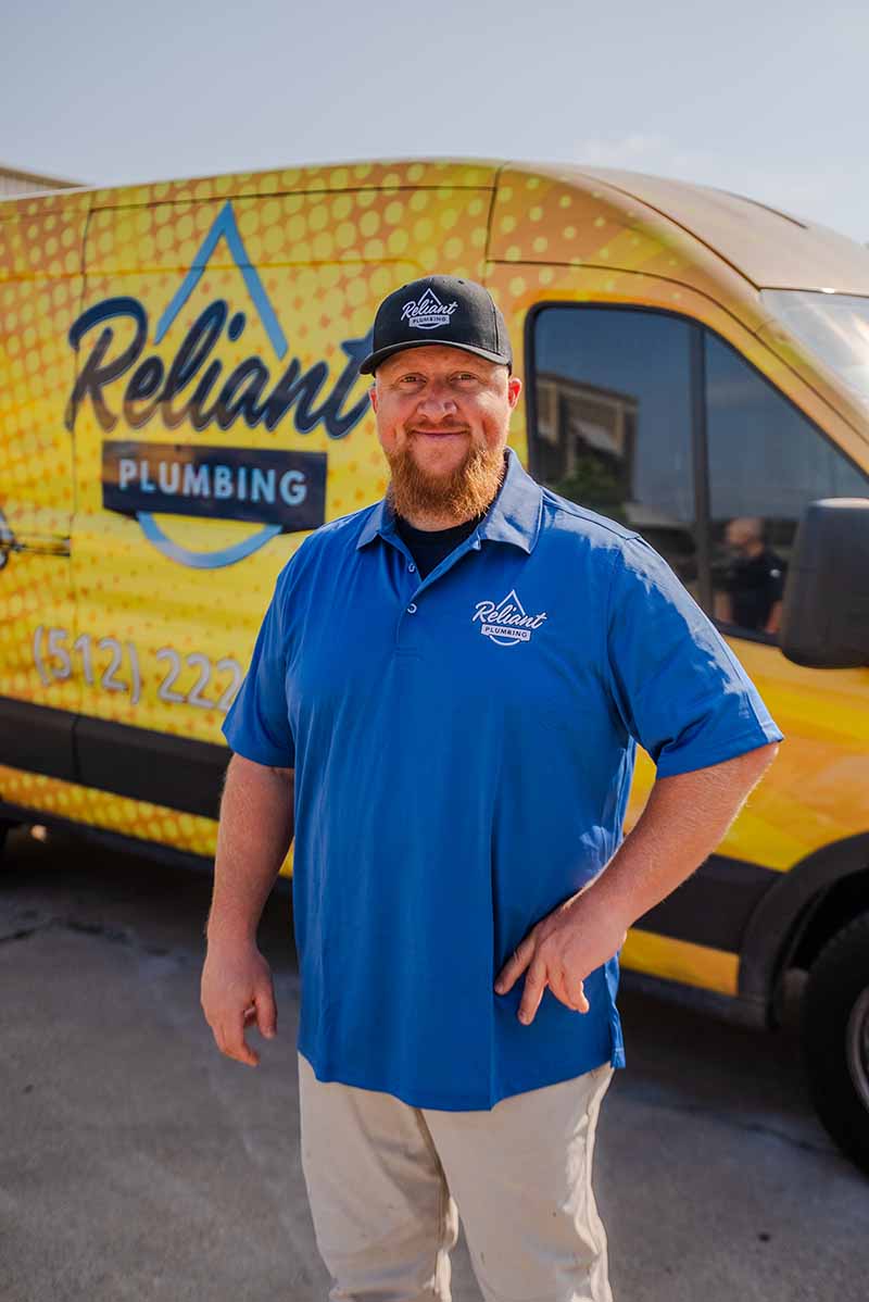 kane childress master plumber at reliant plumbing standing in front of a yellow company vehicle